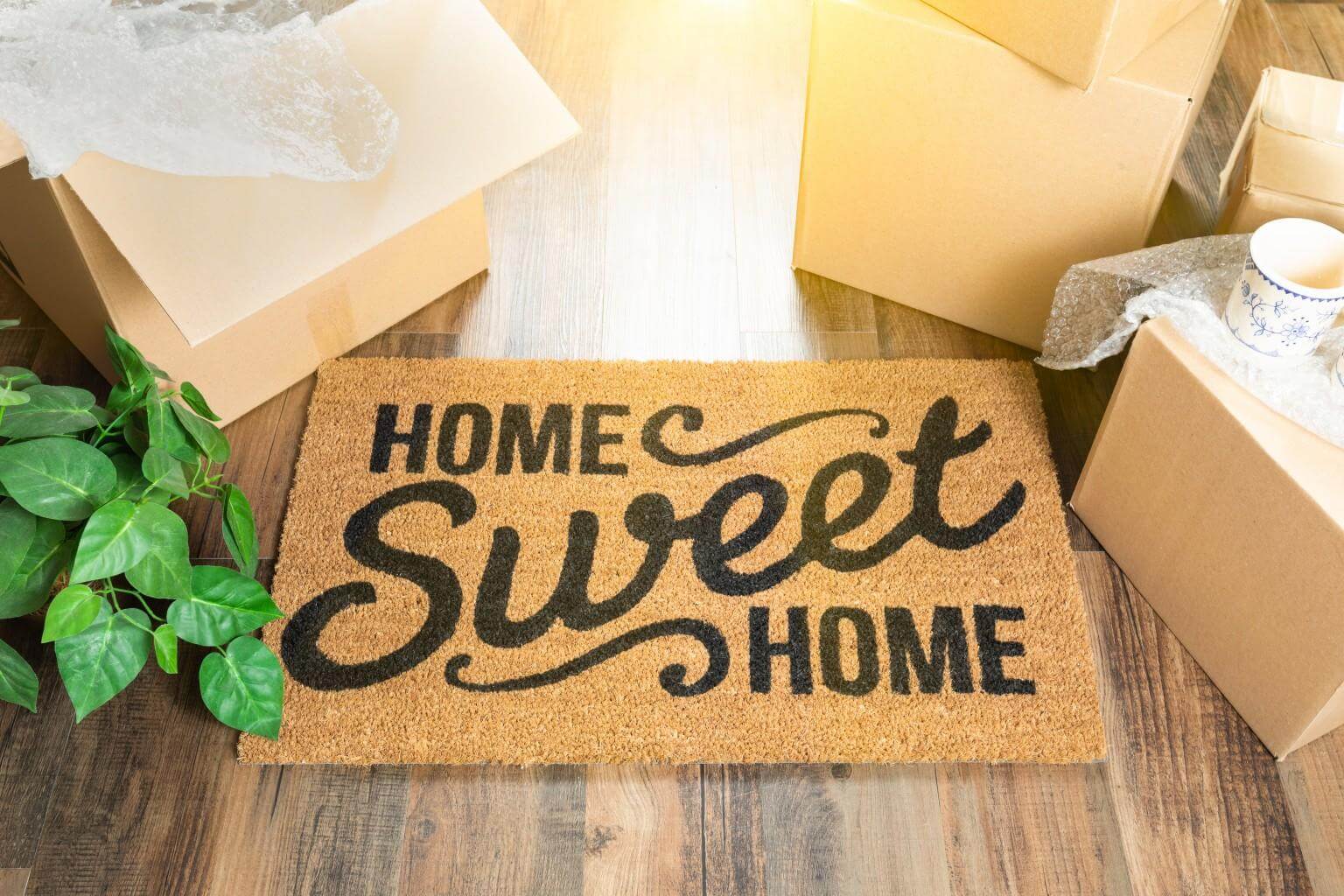 A "Home Sweet Home" doormat sitting next to open cardboard moving boxes on light wood flooring in a new Las Vegas home.