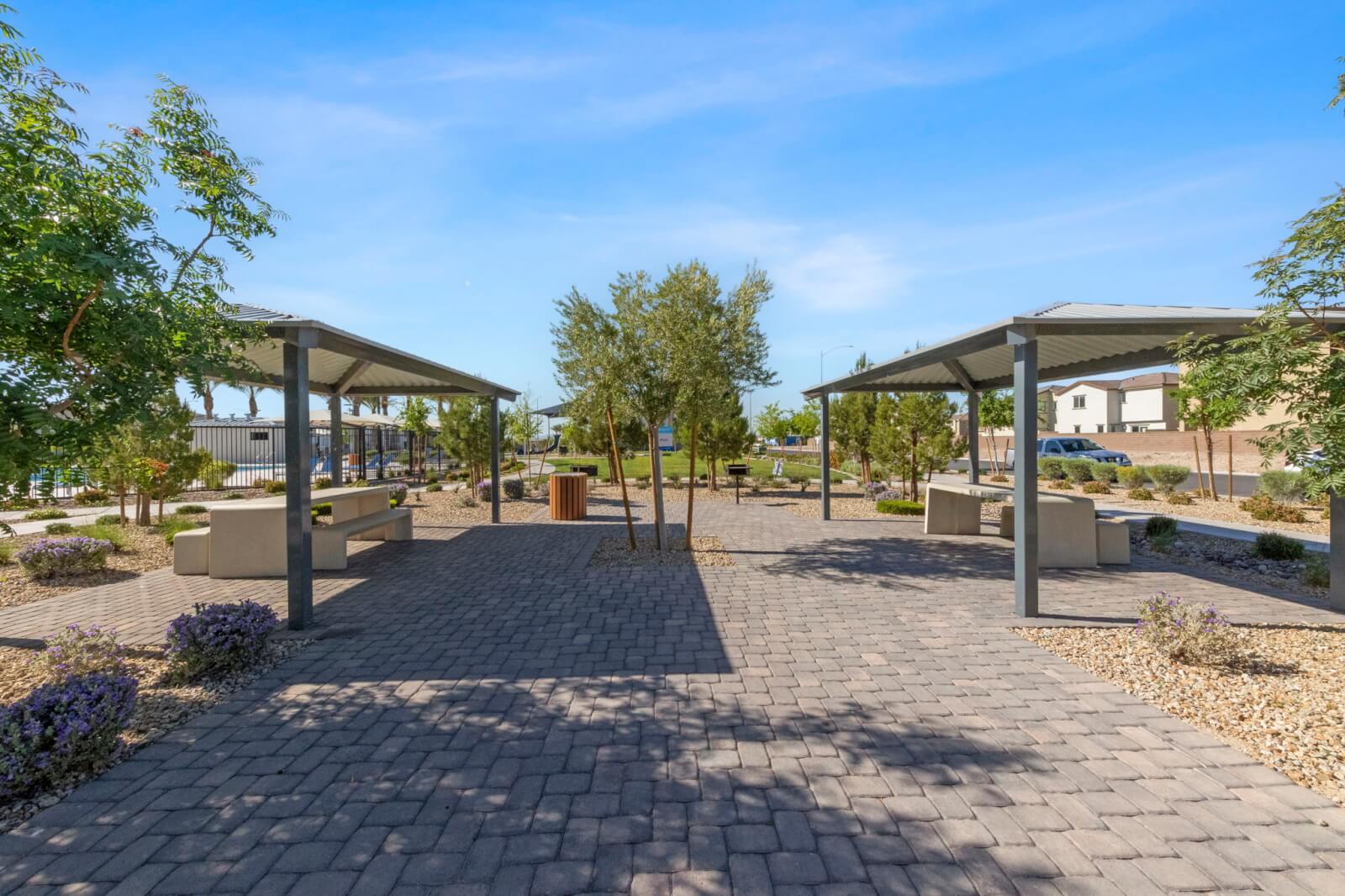 Two shaded picnic pavilions facing a wide paver walkway in a lushly landscaped park at the Watercolor planned community.