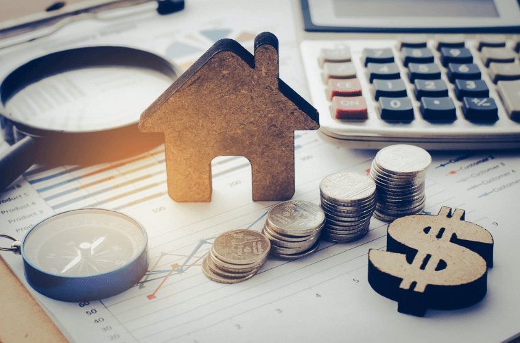 A wooden house cutout sitting next to stacked coins, a compass, and a calculator on a financial chart for a Las Vegas townhome loan.