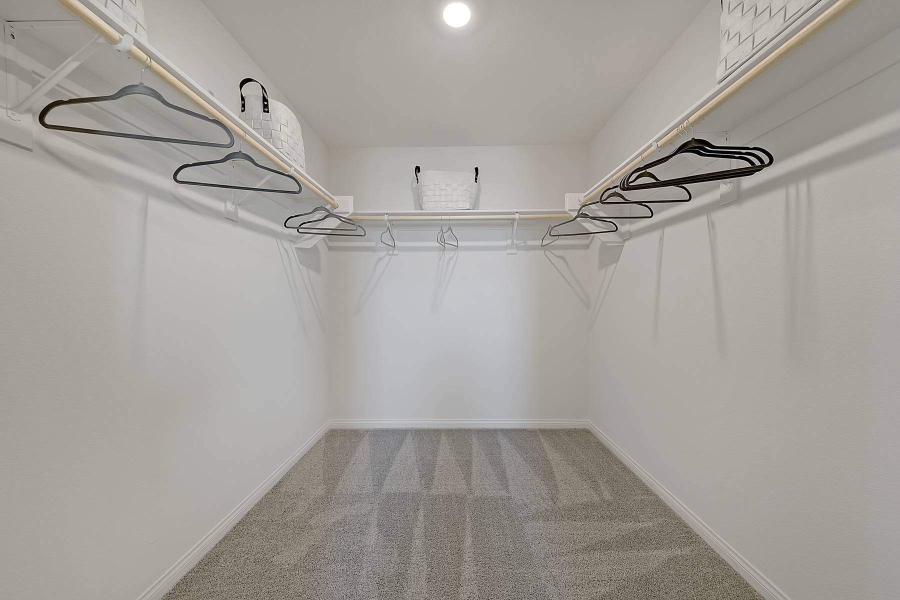 Spacious walk-in closet featuring beige carpeting, white built-in shelving, and wooden clothing rods in a Crimson Plan 520 model home.