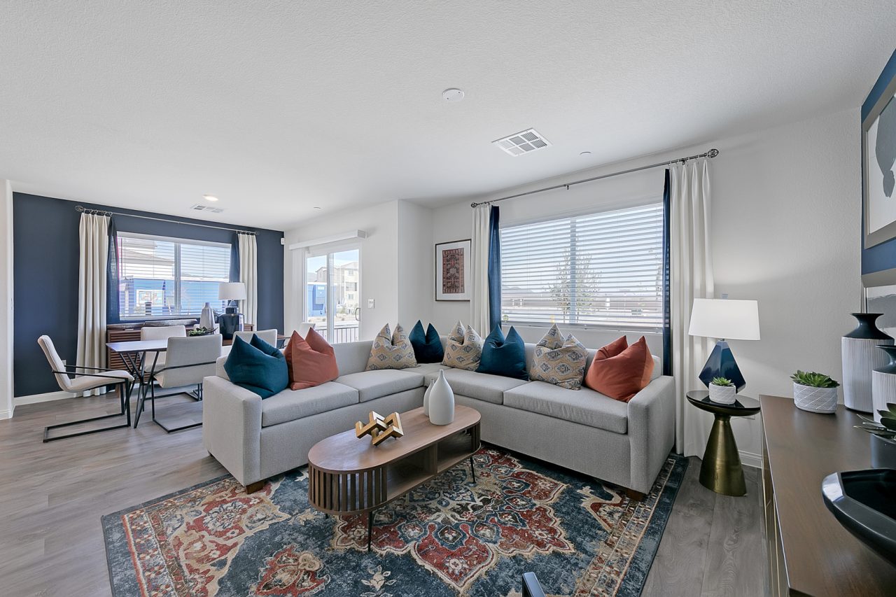 Open-concept living room featuring a grey sectional, upgraded vinyl flooring, a wood coffee table, and a dining area against a dark blue wall in a Crimson Plan 520 model home.