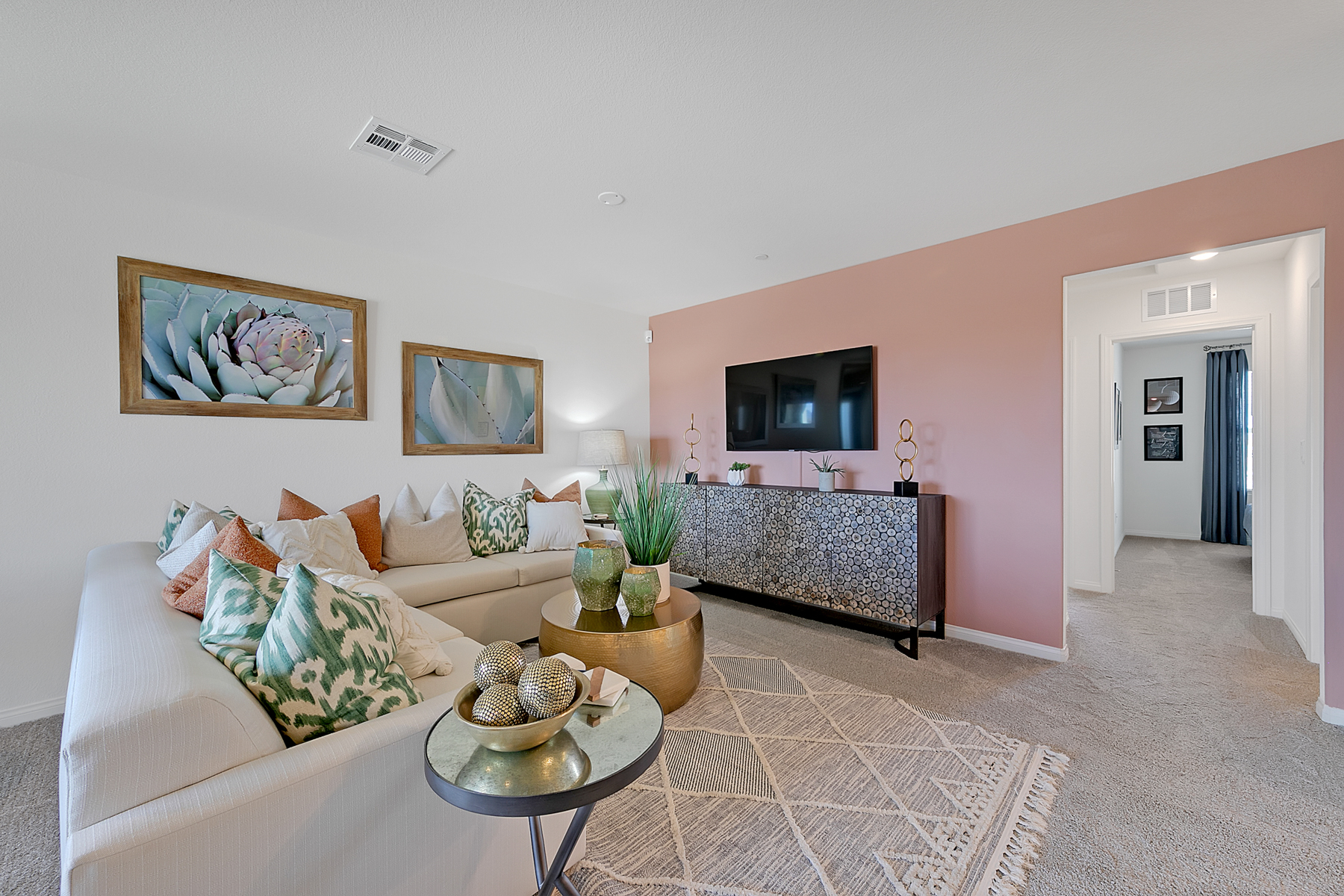 Living room featuring a light sofa, gold coffee tables, a patterned rug, and a media console against a pink accent wall in a Crimson Plan 525 model home.