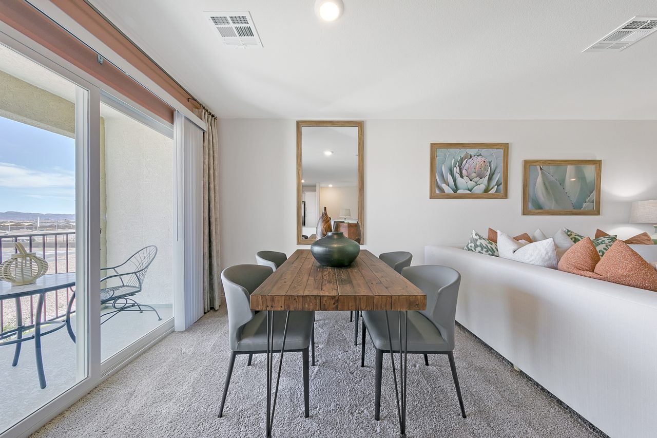 Dining area featuring a wood table with metal legs and grey chairs, adjacent to a living area and sliding glass doors in a Crimson Plan 525 model home.