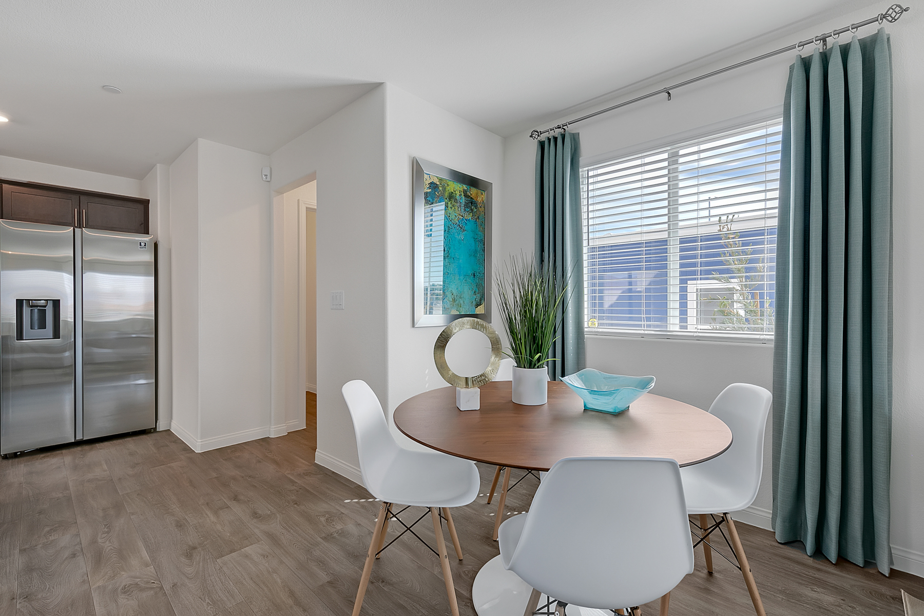 Dining area featuring upgraded vinyl flooring, a round wood table, white chairs, and a view of the kitchen in an Indigo Plan 541 model home.