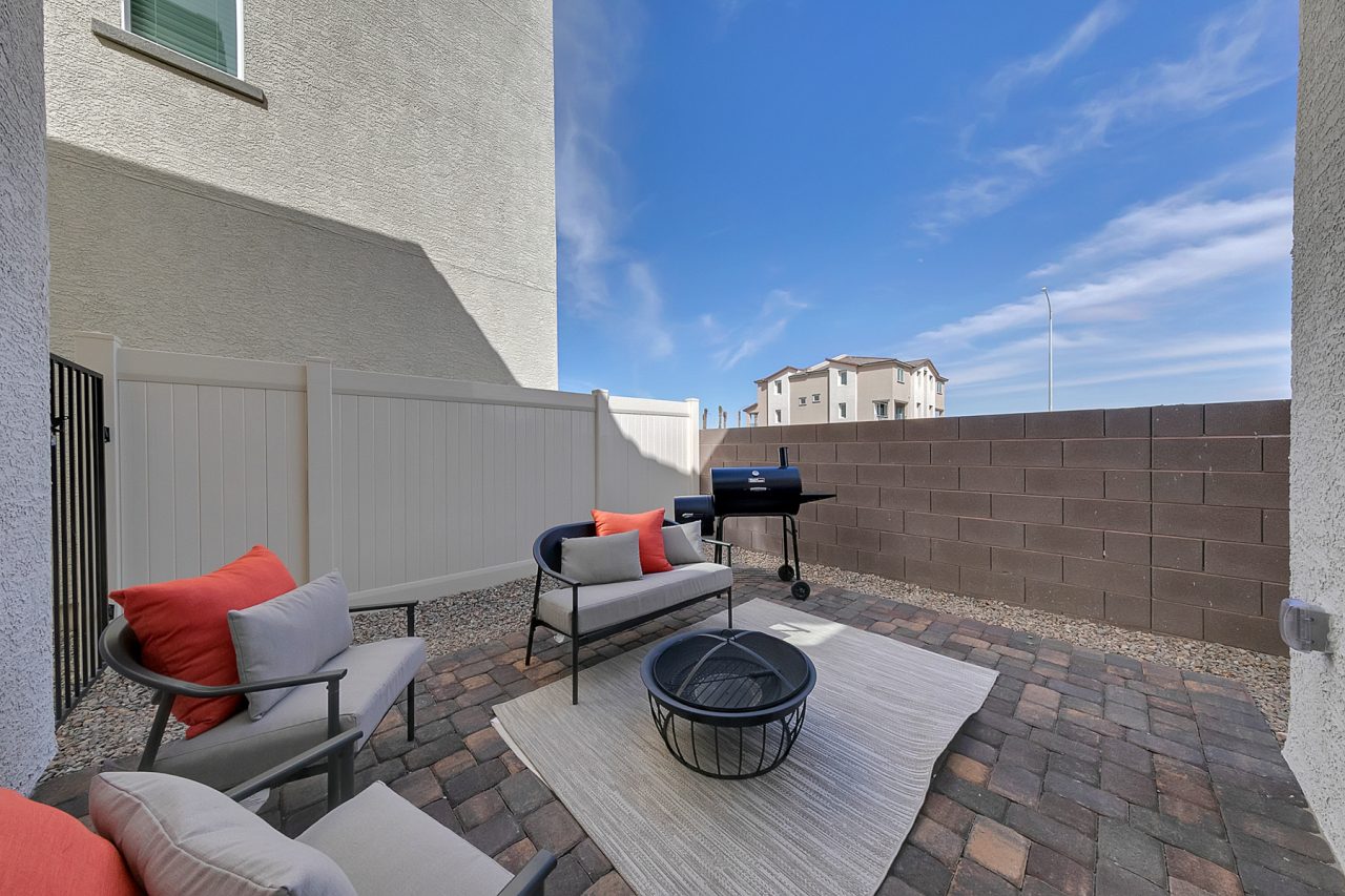 Private backyard patio featuring brick pavers, a fire pit, outdoor seating, and a small grill in an Indigo Plan 541 home.
