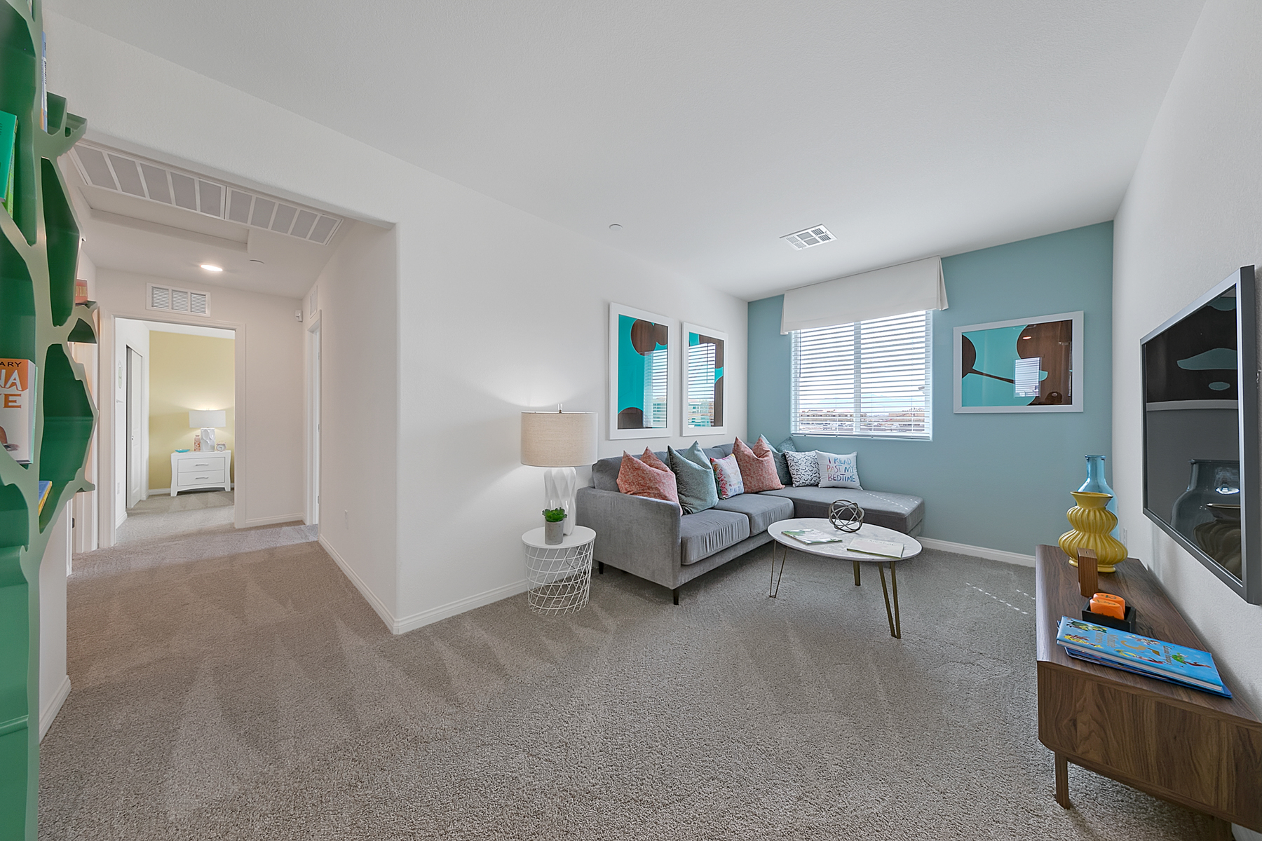 Carpeted loft area featuring a grey sectional sofa, white wire coffee table, and a wood media console in an Indigo Plan 541 model home.