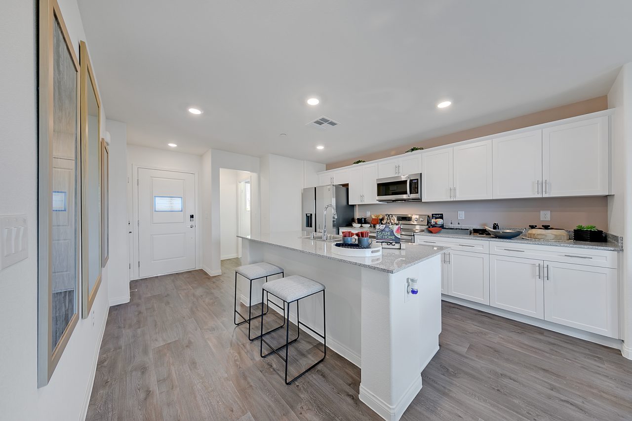 Modern kitchen featuring upgraded vinyl flooring, white cabinetry, granite countertops, and stainless steel Samsung® appliances in an Indigo Plan 542 model home.