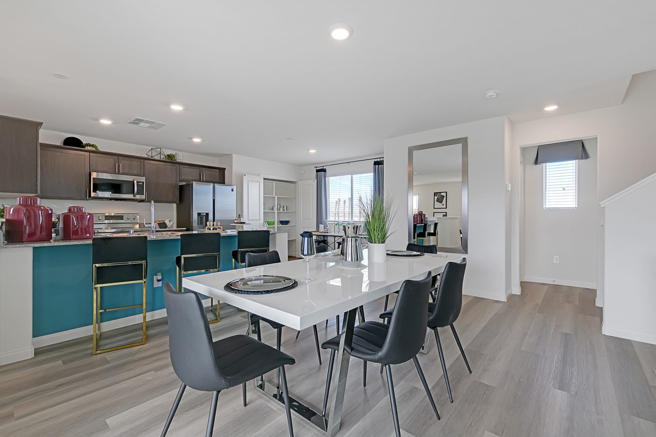Open-concept dining and kitchen area featuring upgraded vinyl flooring, a white table, teal island, granite countertops, and stainless steel Samsung® appliances in an Indigo Plan 543 model home.