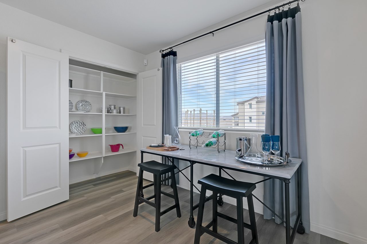 Large pantry featuring white shelving, adjacent to a high table with black stools and upgraded vinyl flooring in an Indigo Plan 543 model home.