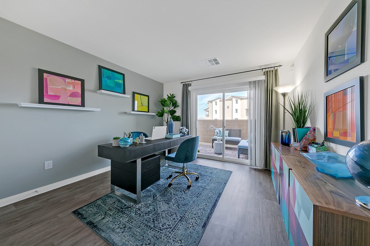 Bonus room configured as an office featuring upgraded vinyl flooring, a black desk, blue chair, and a sliding glass door in an Indigo Plan 543 model home.