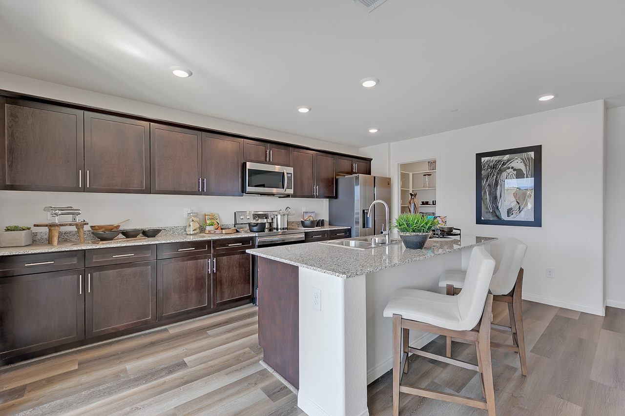 Modern kitchen featuring dark wood cabinetry, granite countertops, an island with seating, upgraded vinyl flooring, and stainless steel Samsung® appliances in an Indigo Plan 544 model home.