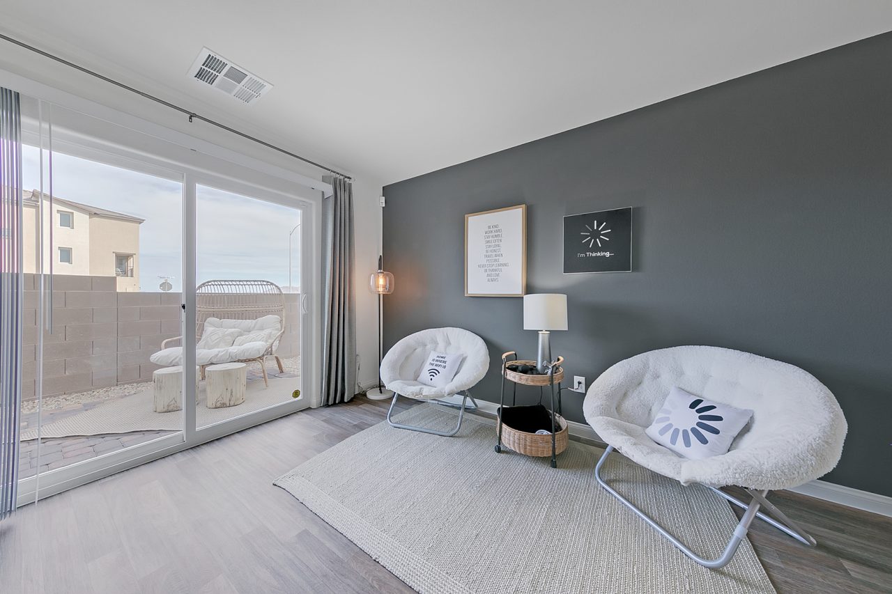 Bonus room featuring upgraded vinyl flooring, a dark grey accent wall, two white saucer chairs, and a sliding glass door in an Indigo Plan 544 model home.