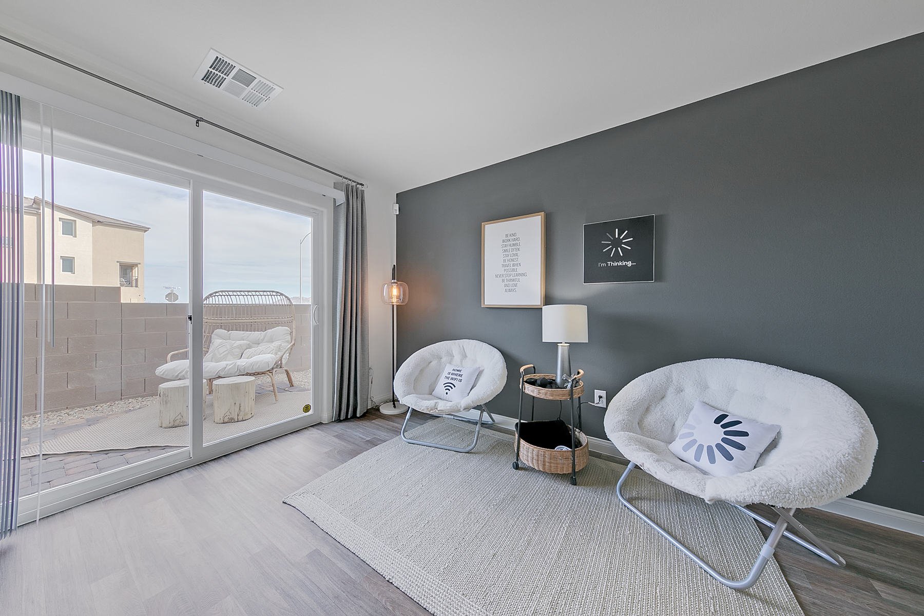 Bonus room featuring upgraded vinyl flooring, a dark grey accent wall, two white saucer chairs, and a sliding glass door in an Indigo Plan 544 model home.