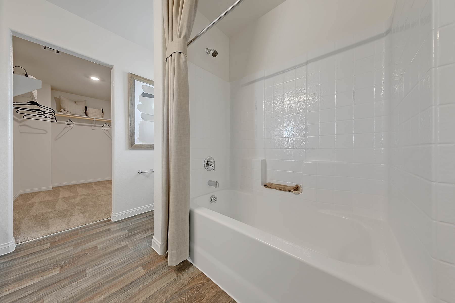 Primary bathroom featuring upgraded vinyl flooring, a white shower-tub combo, and an attached walk-in closet in an Indigo Plan 544 model home.