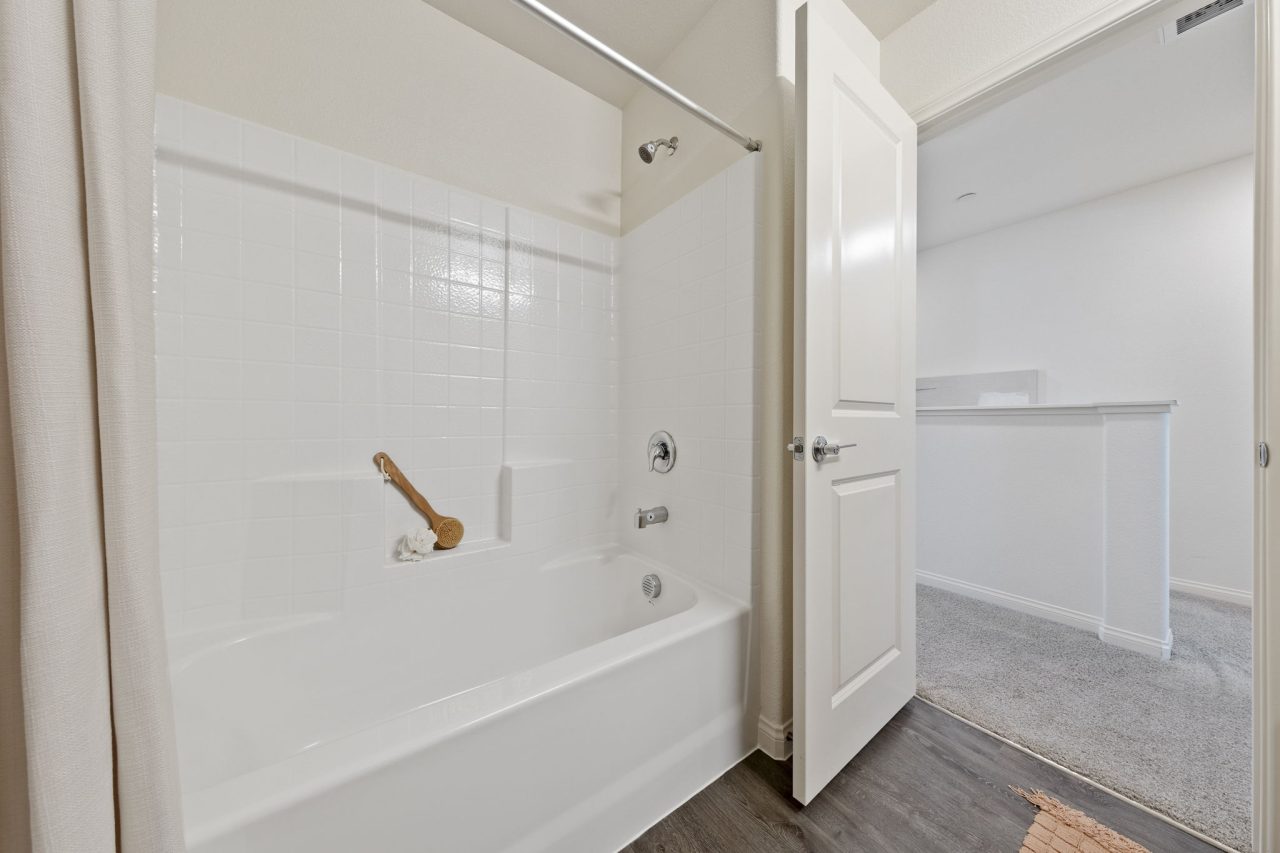 Styled secondary guest bathroom with light wood-look upgraded vinyl plank flooring, a grey single quartz vanity, and a shower-tub with a modern geometric blue and grey curtain.