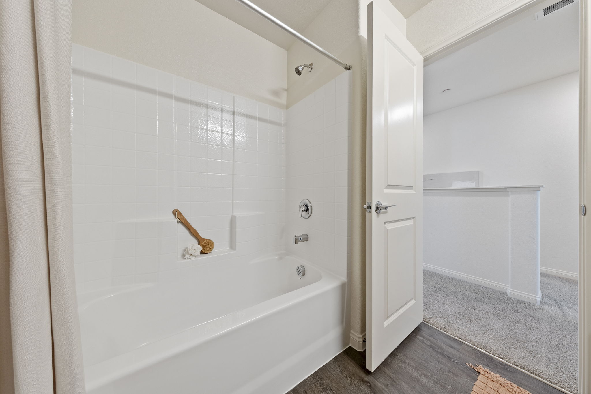 Styled secondary guest bathroom with light wood-look upgraded vinyl plank flooring, a grey single quartz vanity, and a shower-tub with a modern geometric blue and grey curtain.
