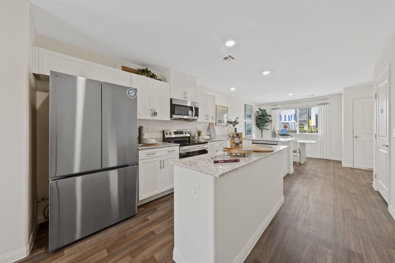 Modern open-concept kitchen featuring white cabinetry, a granite island, upgraded vinyl flooring, and stainless steel Samsung® appliances in a Solaris model home.