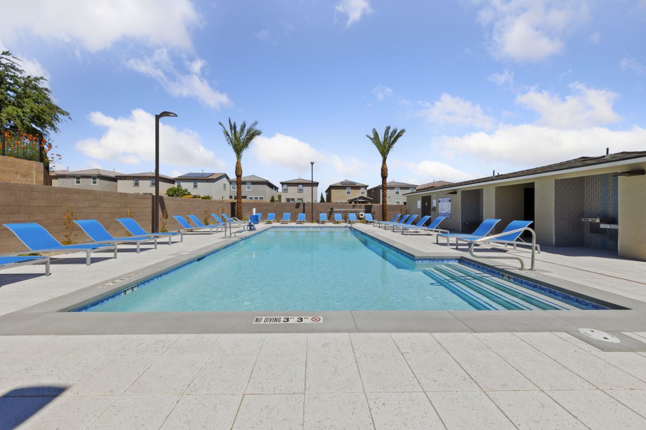 Sparkling rectangular community swimming pool surrounded by bright blue lounge chairs and palm trees at the Solaris new home community.