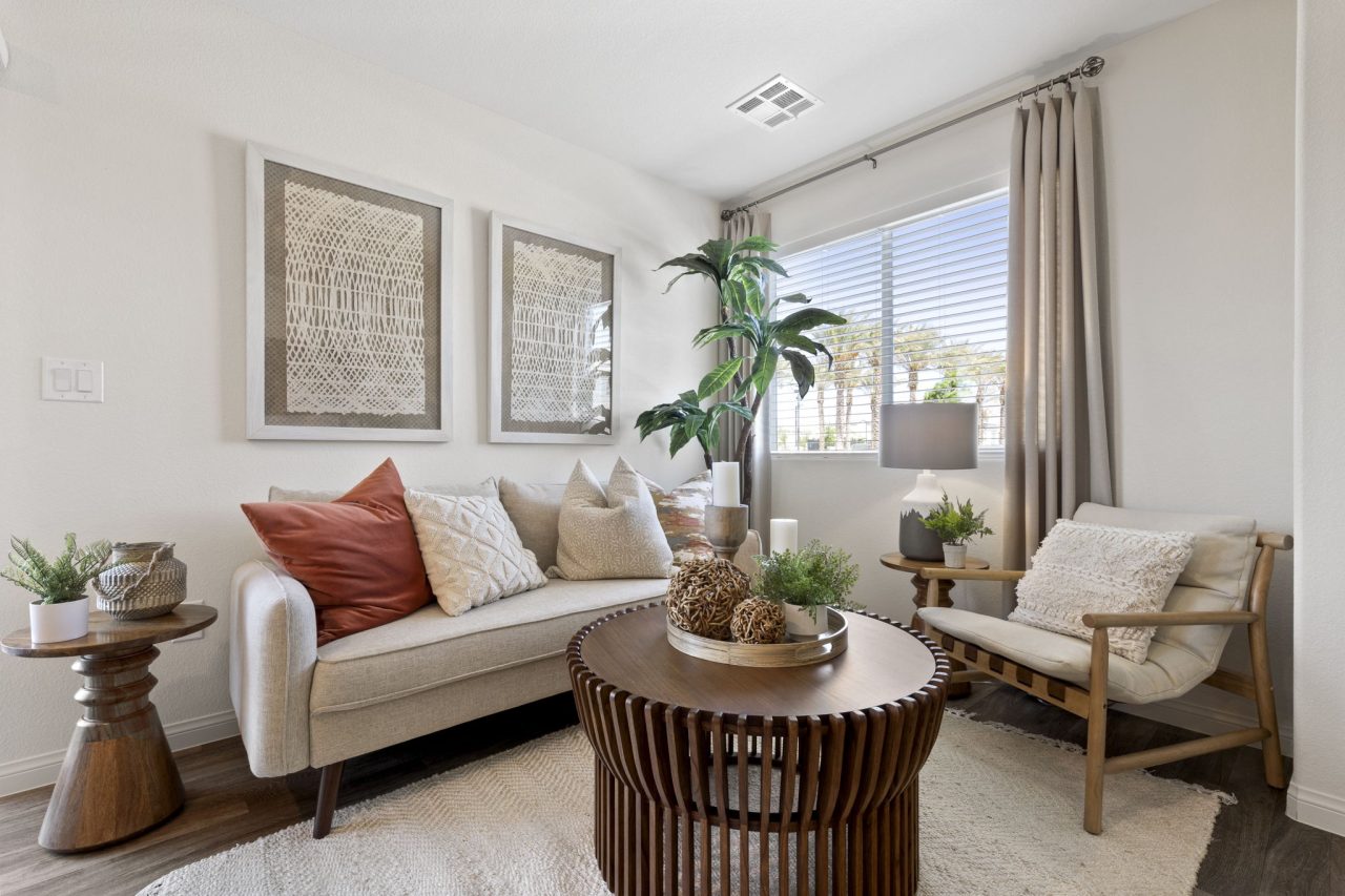 Living room featuring upgraded vinyl flooring, a light beige sofa, slatted wood coffee table, and large framed artwork in a Sienna model home.