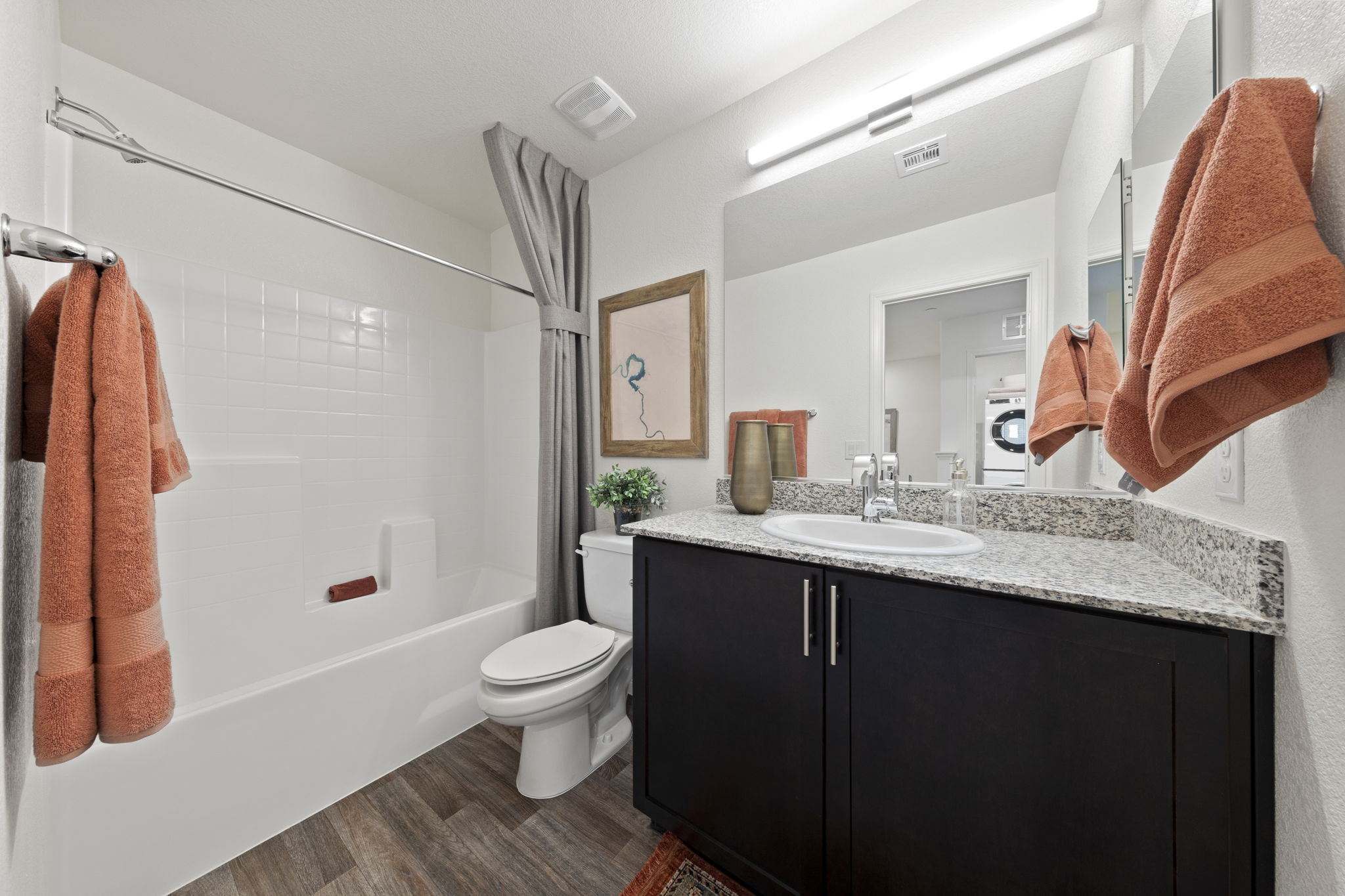 Full bathroom featuring upgraded vinyl flooring, a dark wood vanity with granite countertops, and a white shower-tub combination in a Sienna model home.