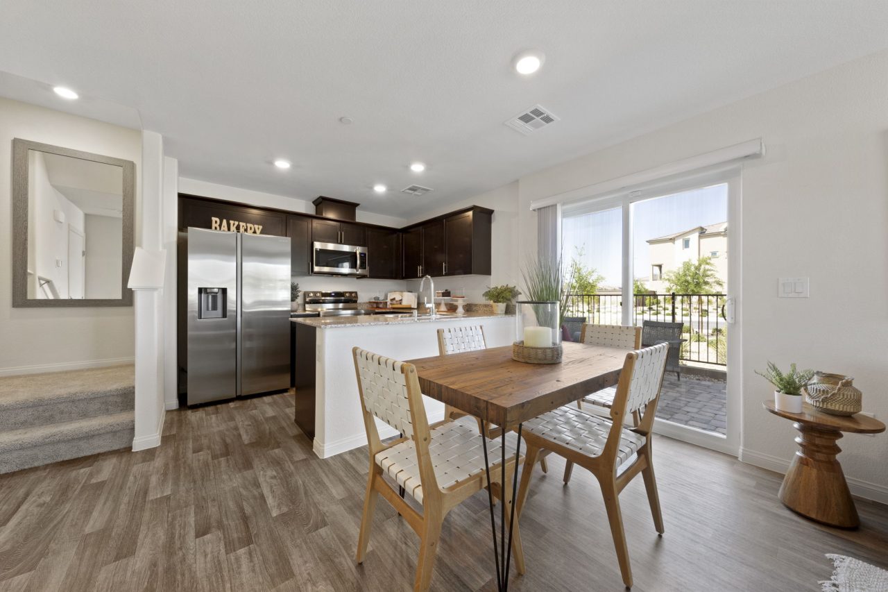 Dining and kitchen area featuring upgraded vinyl flooring, a wood dining table, dark kitchen cabinets, granite countertops, and stainless steel Samsung® appliances in a Sienna model home.