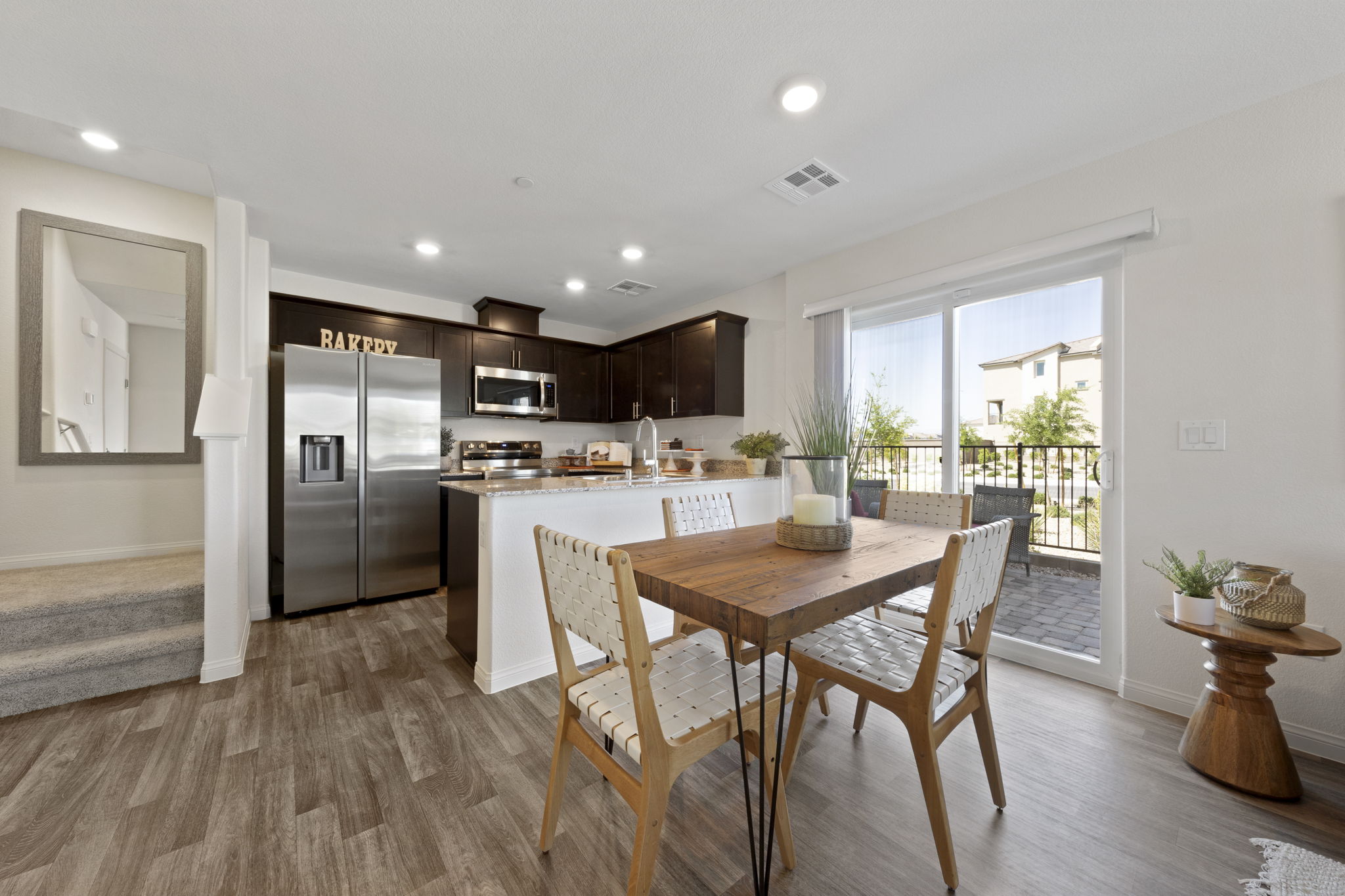 Dining and kitchen area featuring upgraded vinyl flooring, a wood dining table, dark kitchen cabinets, granite countertops, and stainless steel Samsung® appliances in a Sienna model home.
