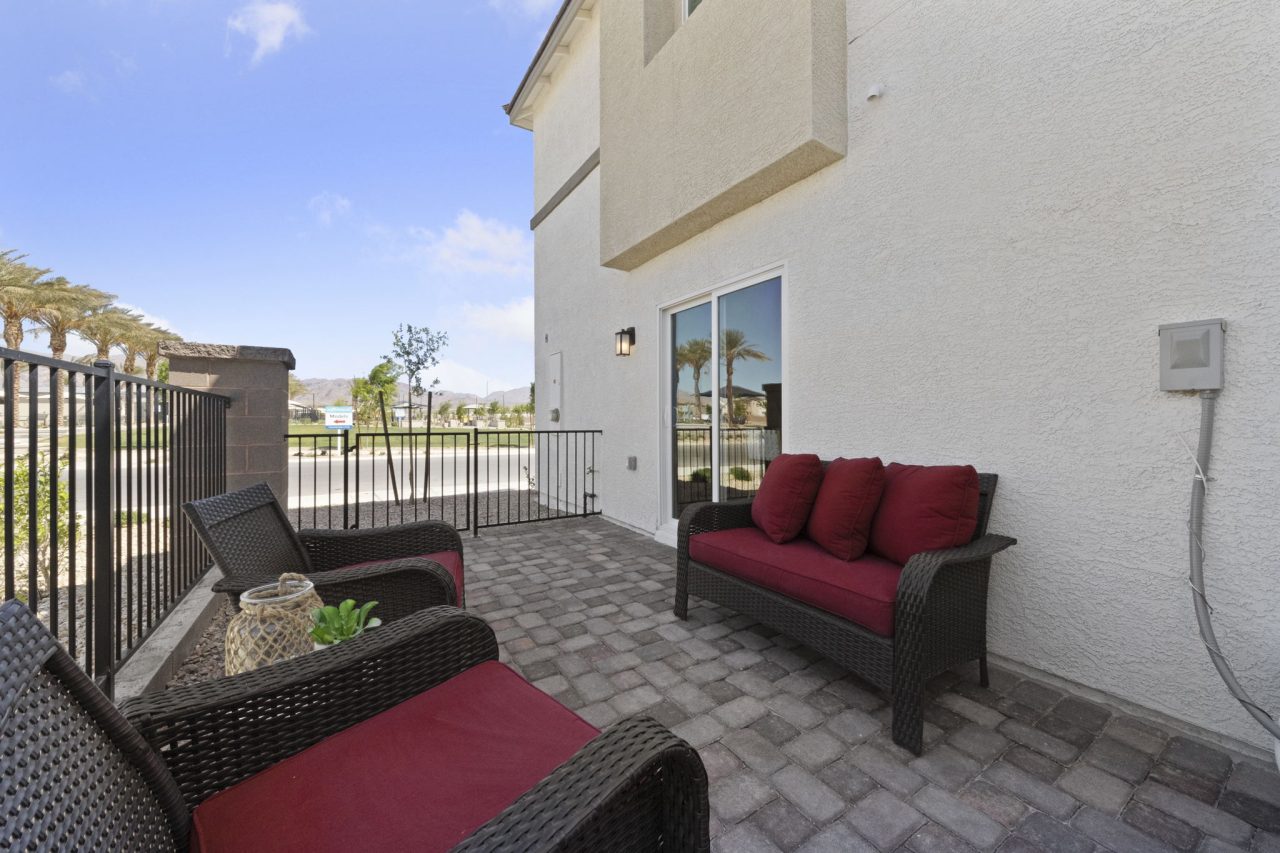 Private paver patio featuring dark wicker outdoor furniture with red cushions at a Sienna model home in the Watercolor planned community.