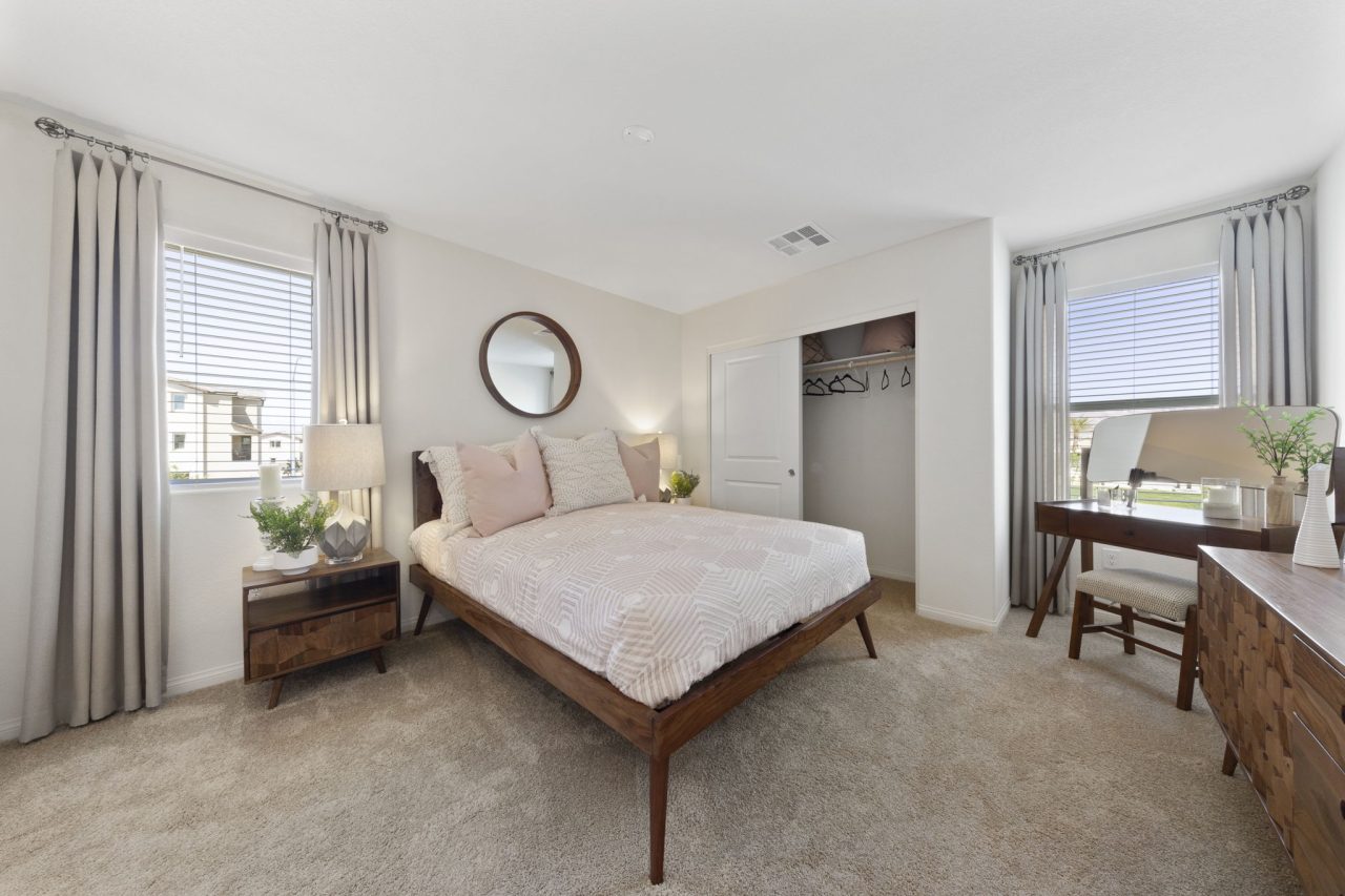 Primary bedroom featuring a wood bed frame, a vanity desk, beige carpeting, and an open closet in a Sienna model home.