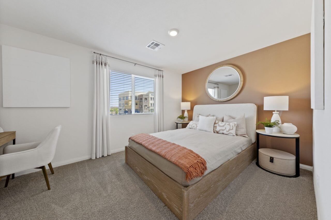 Secondary bedroom featuring a terracotta accent wall, a light wood bed with a rust-orange throw blanket, and a dedicated desk area in a Solaris model home.
