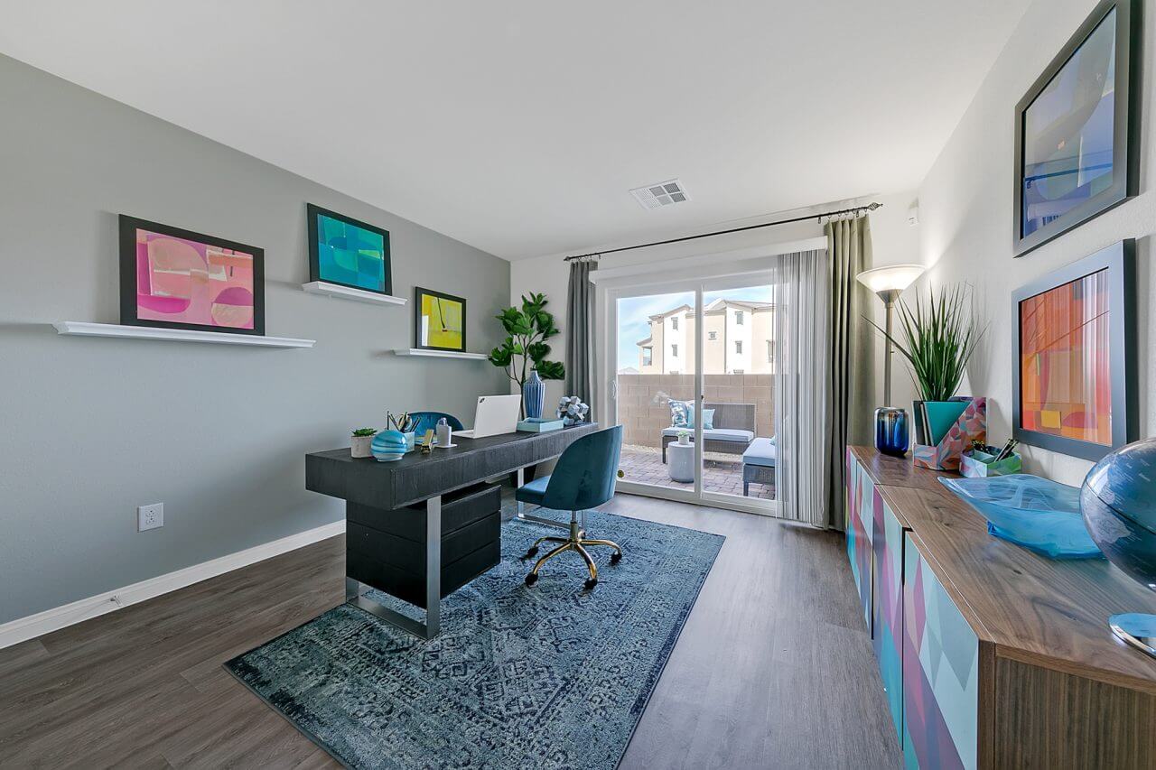 Bonus room configured as an office featuring upgraded vinyl flooring, a black desk, blue chair, and a sliding glass door in an Indigo Plan 543 model home.