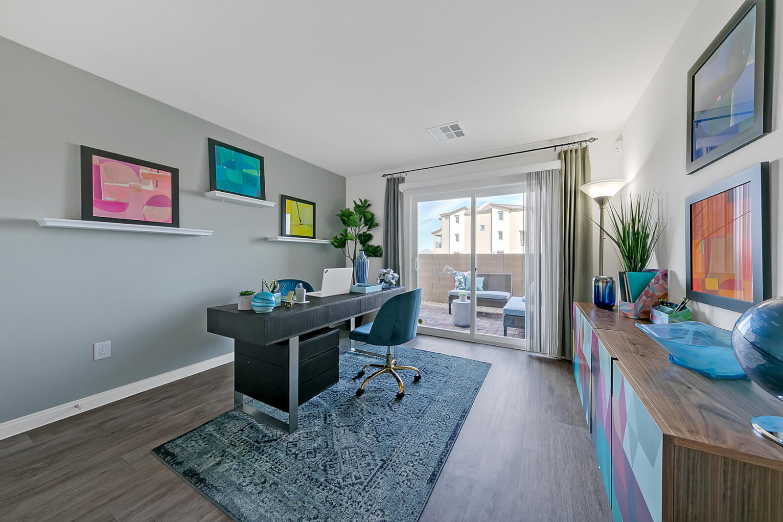Bonus room configured as an office featuring upgraded vinyl flooring, a black desk, blue chair, and a sliding glass door in an Indigo Plan 543 model home.