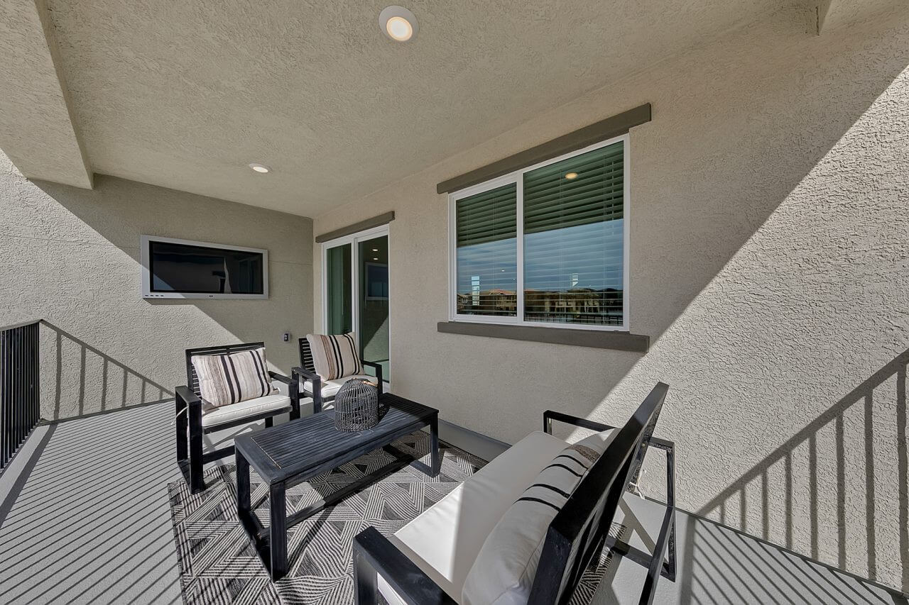 Oversized covered balcony featuring outdoor seating, a black coffee table, and a wall-mounted television in an Indigo Plan 543 model home at the Watercolor neighborhood.
