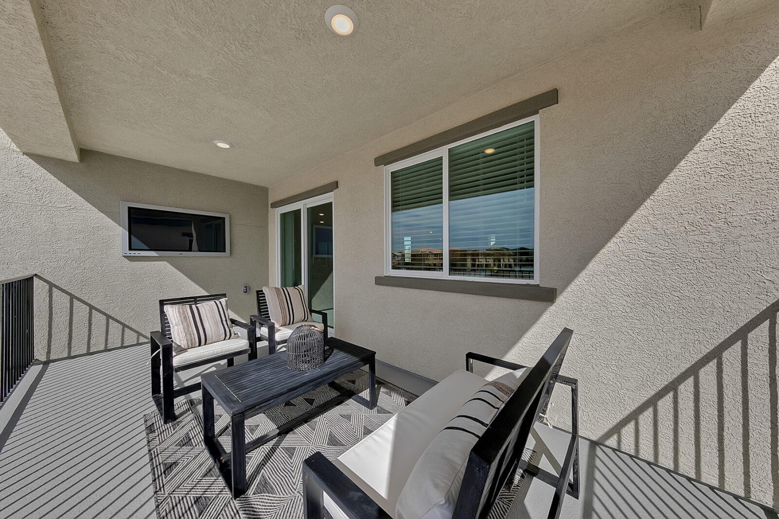 Oversized covered balcony featuring outdoor seating, a black coffee table, and a wall-mounted television in an Indigo Plan 543 model home at the Watercolor neighborhood.