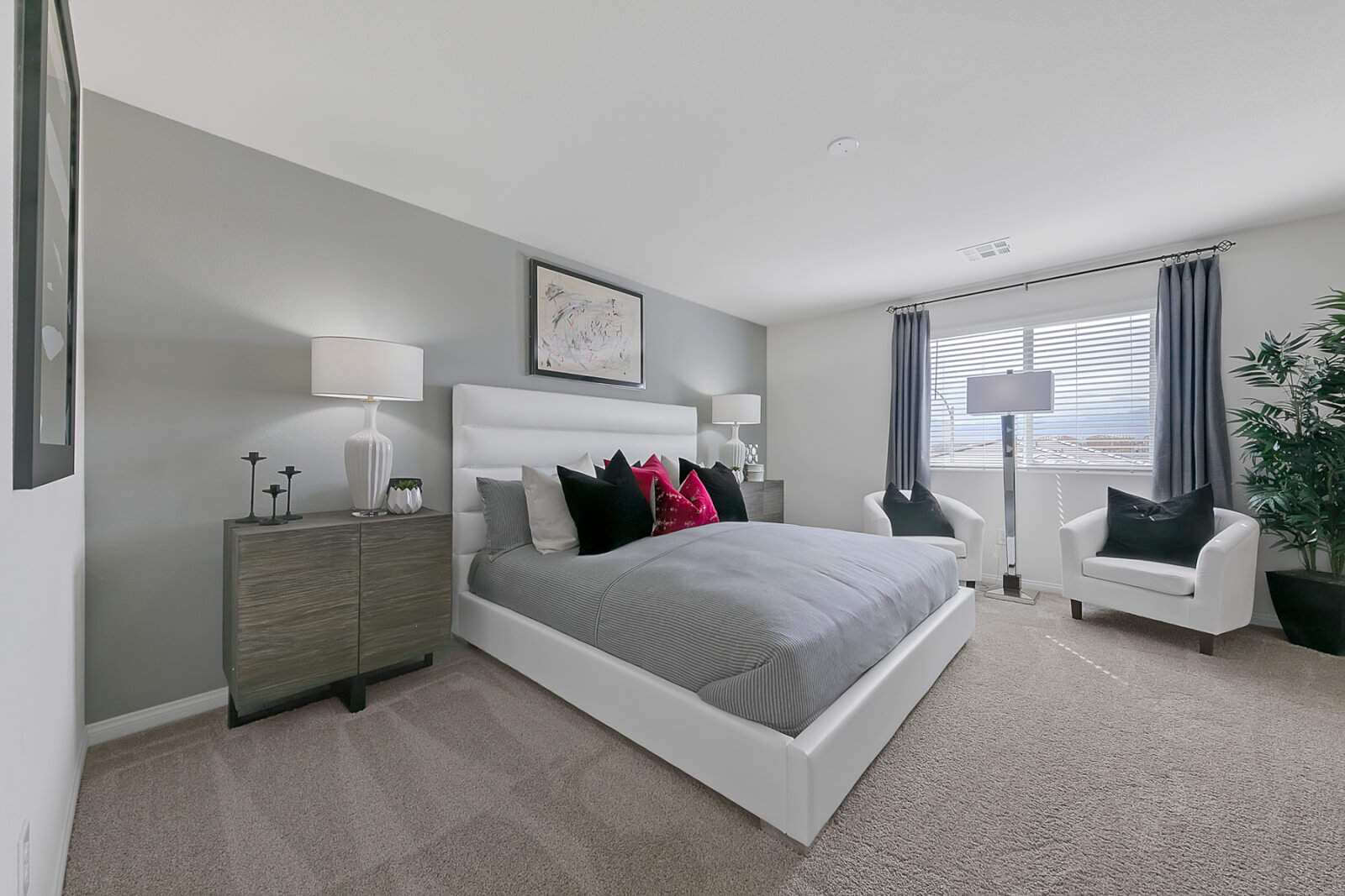 Primary bedroom featuring a white upholstered bed, grey dresser, two white armchairs, and a grey accent wall in an Indigo Plan 543 model home.