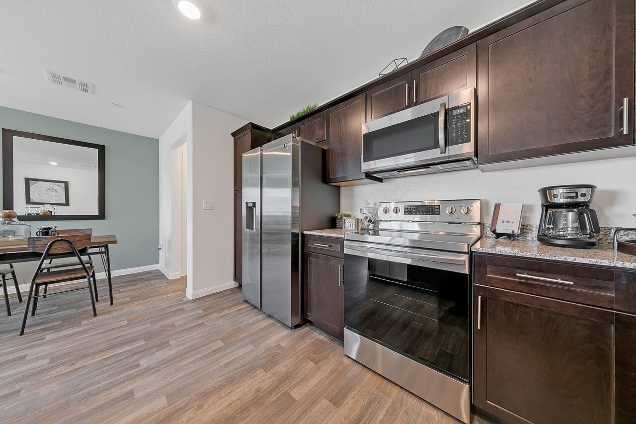 Kitchen featuring dark wood cabinets, granite countertops, upgraded vinyl flooring, and stainless steel Samsung® appliances in a Crimson Plan 523 model townhome.