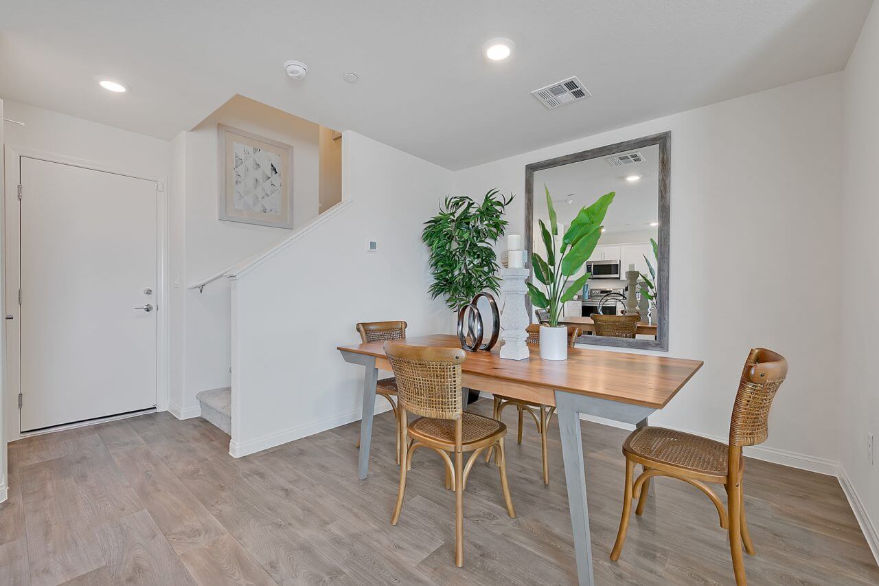 Dining area featuring upgraded vinyl flooring, a wood table with grey legs, woven chairs, and a large floor mirror in a Crimson Plan 524 model townhome.