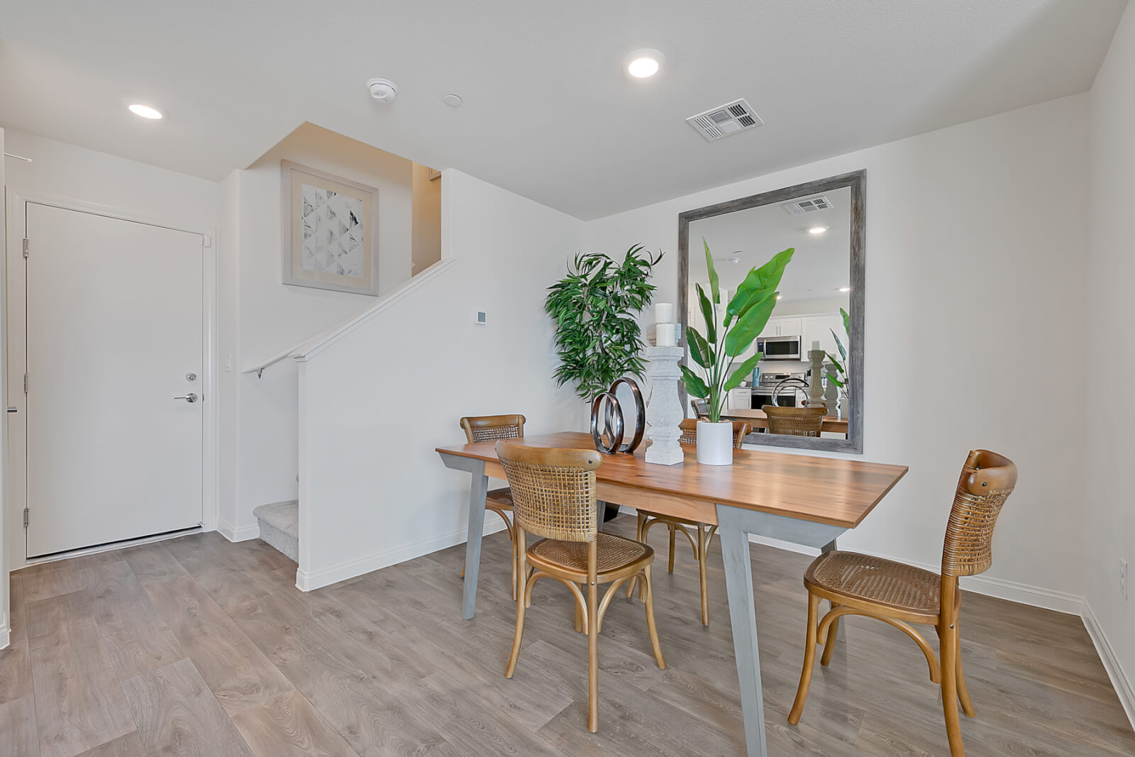 Dining area featuring upgraded vinyl flooring, a wood table with grey legs, woven chairs, and a large floor mirror in a Crimson Plan 524 model townhome.