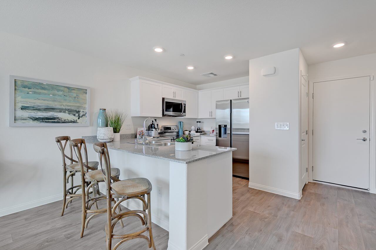 Modern kitchen inside the Crimson Plan 524 townhome at Watercolor in North Las Vegas, featuring white cabinetry, granite countertops, and a kitchen island with woven barstools.