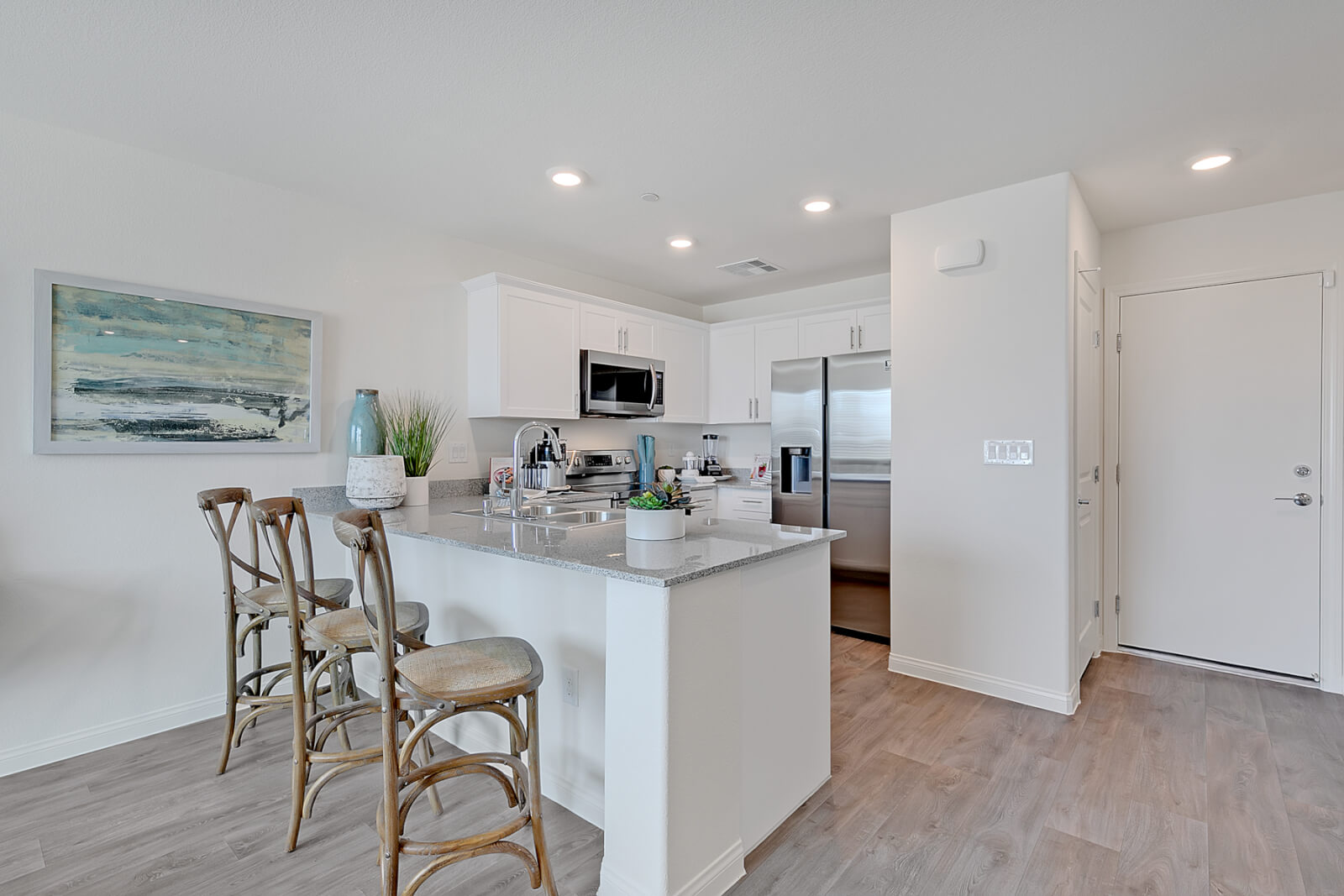 Modern kitchen inside the Crimson Plan 524 townhome at Watercolor in North Las Vegas, featuring white cabinetry, granite countertops, and a kitchen island with woven barstools.