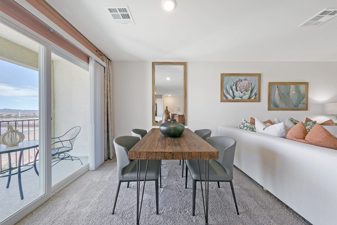 Modern dining room inside the Crimson Plan 525 model townhome at Watercolor in North Las Vegas, featuring a rustic wood table and sliding glass doors to a patio.