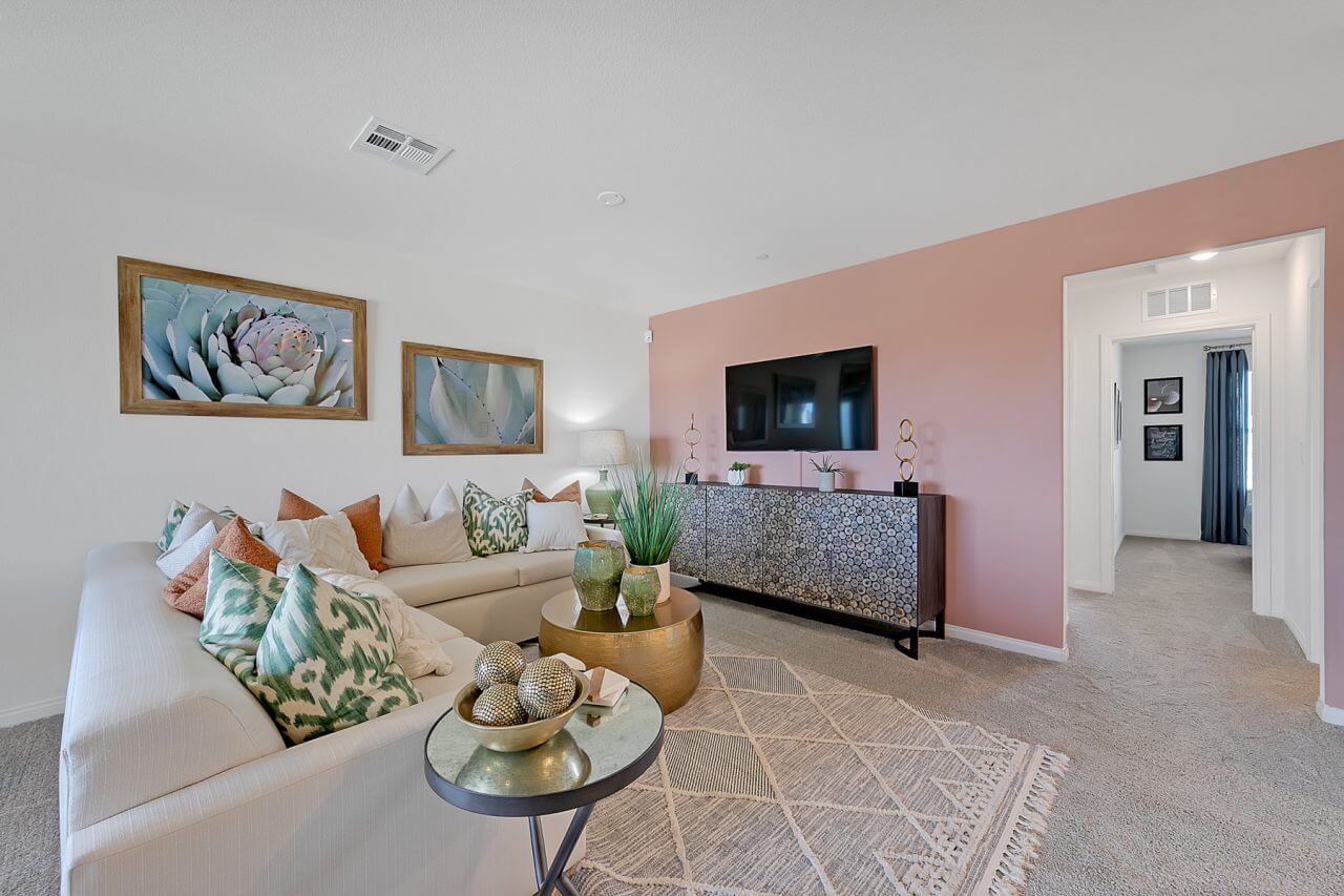 Modern living room inside the Crimson Plan 525 townhome at Watercolor in North Las Vegas, featuring a light sofa, pink accent wall, and gold coffee tables.
