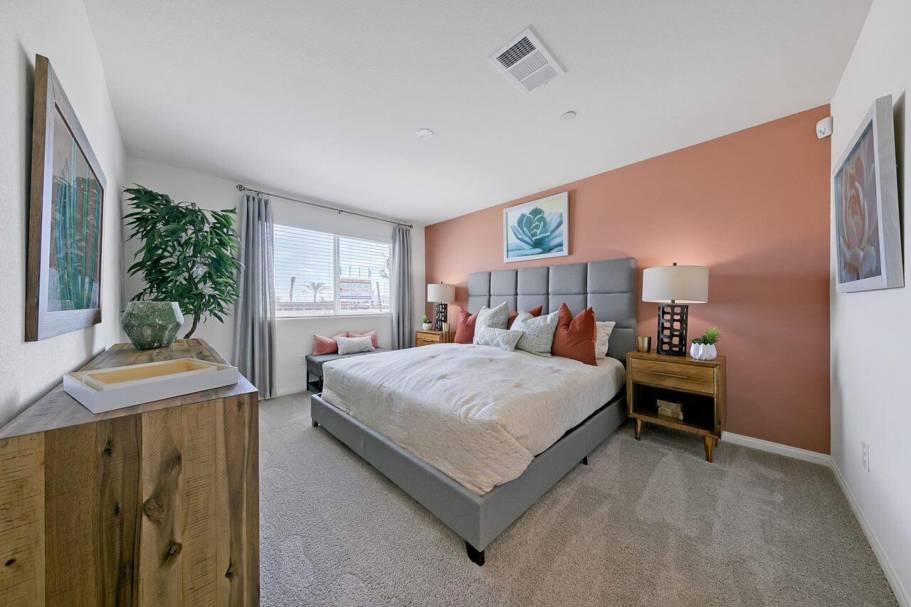 Spacious primary bedroom inside the Crimson Plan 525 townhome at Watercolor in North Las Vegas, featuring a coral accent wall and grey upholstered bed.