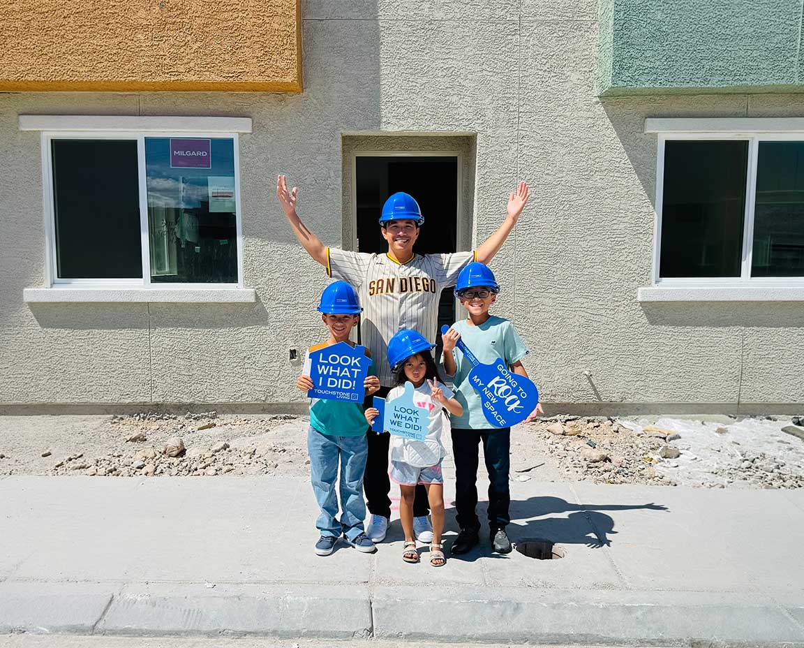 a dad and three kids posing in hard hats and signs in front of a new house all happy