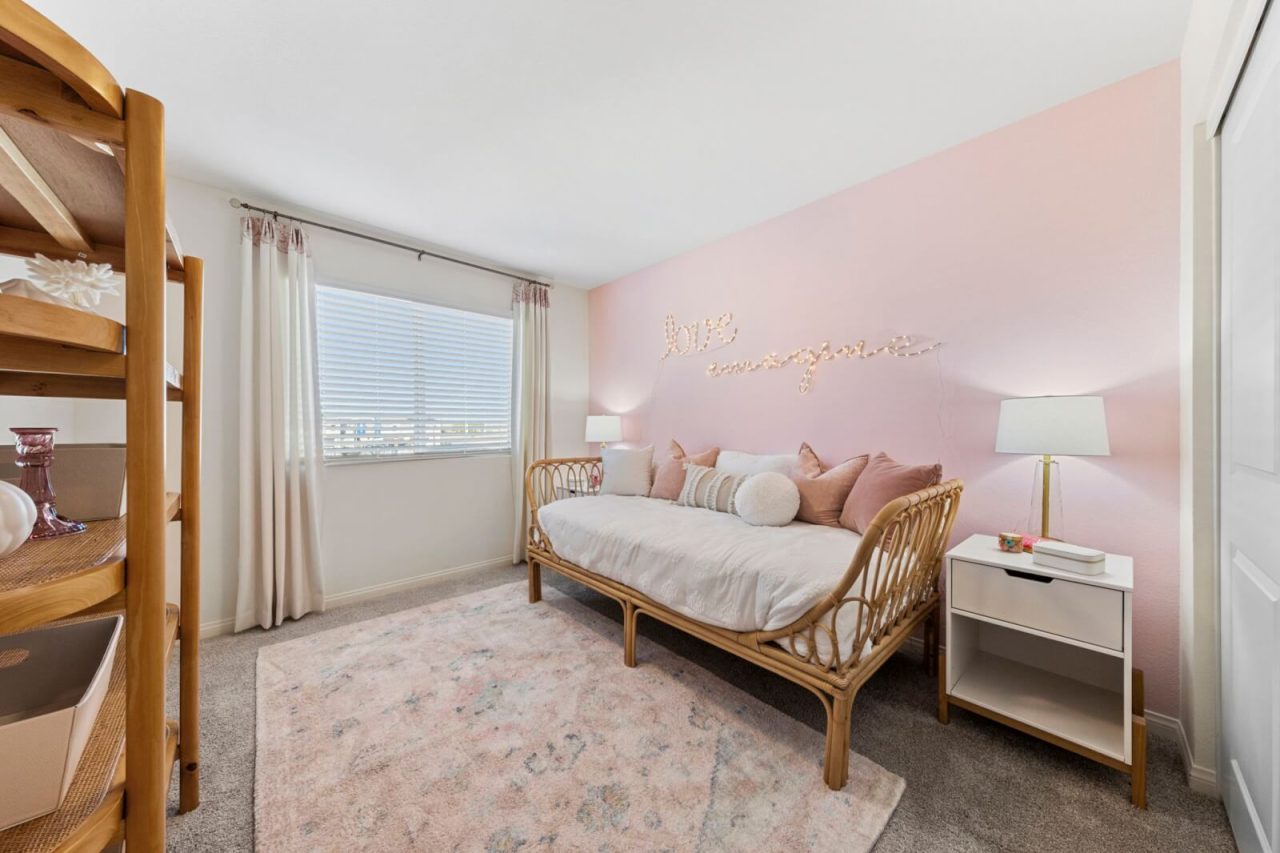 Charming secondary bedroom featuring a pink accent wall, a rattan daybed, and light-colored decor in a Touchstone Living home.