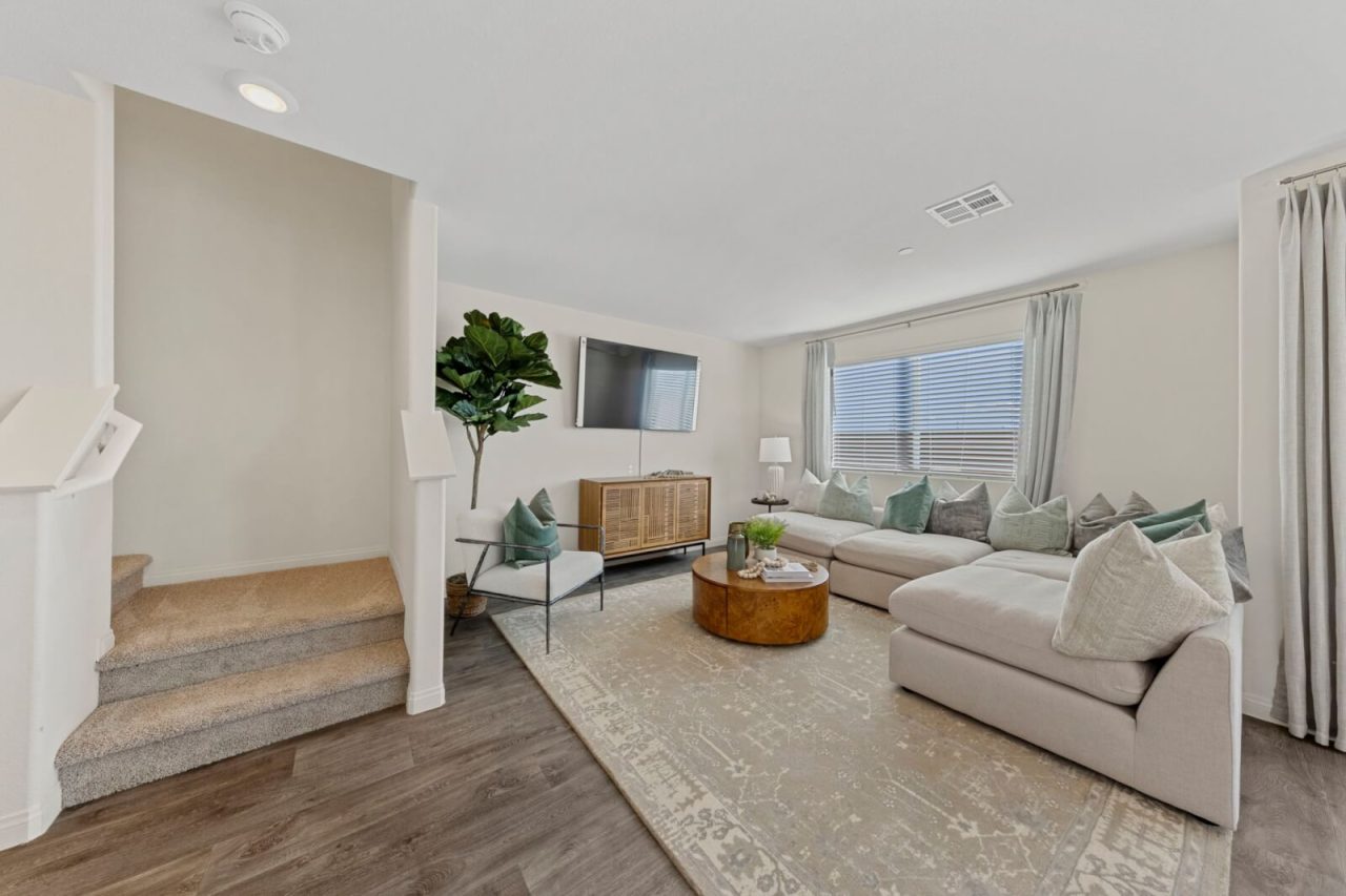 Modern living room featuring vinyl flooring, a large beige sectional sofa, and carpeted stairs leading upstairs in a Touchstone Living home at Independence.