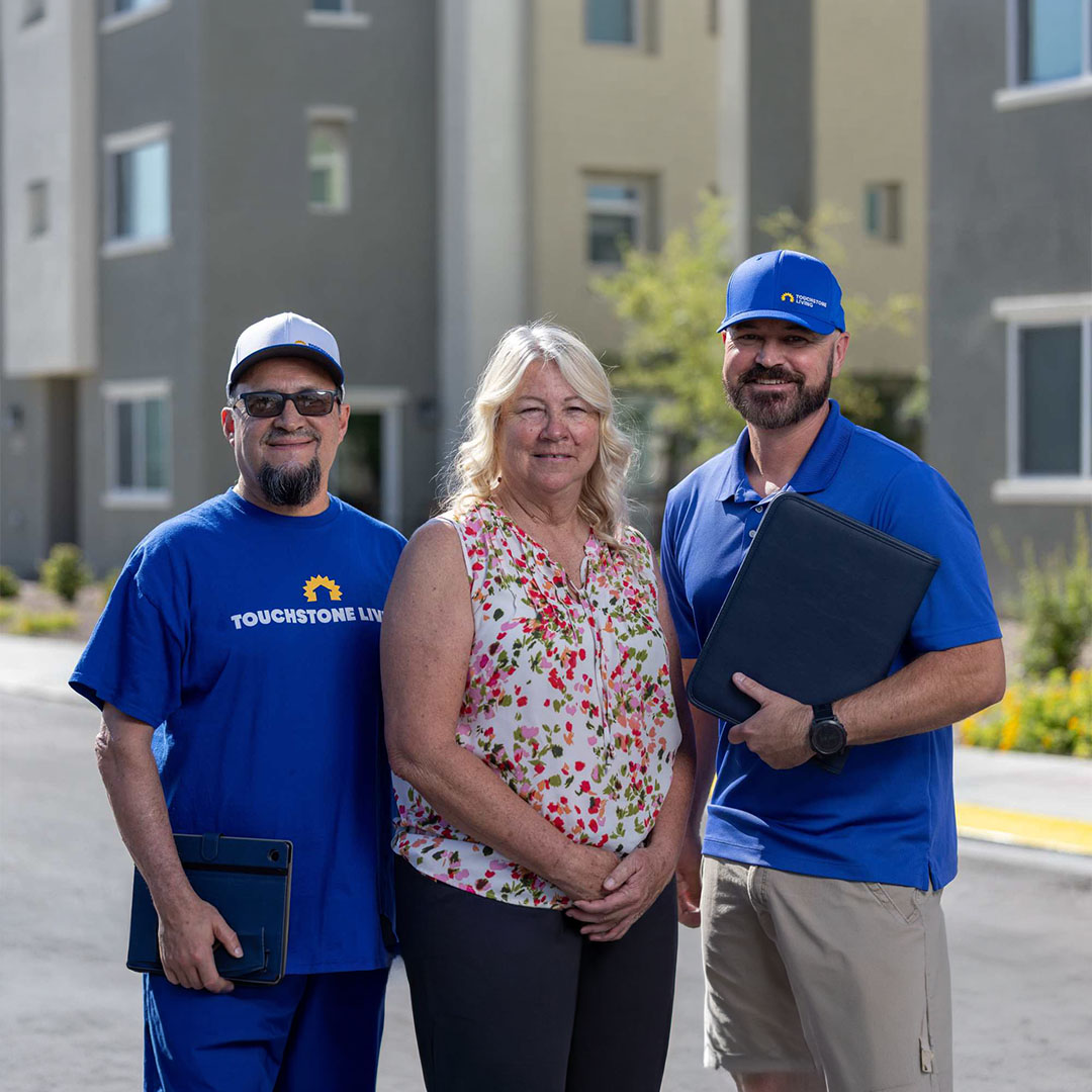 Two Touchstone employees posing with a new homeowner buyer in front of buildings